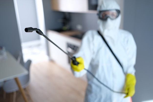 Person in protective suit and mask disinfects kitchen. Destruction of bedbugs and cockroaches in apartment concept