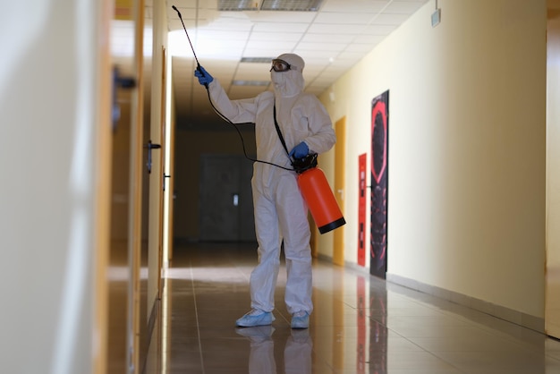 person in protective suit with disinfectant cleaning public area in building during pandemic