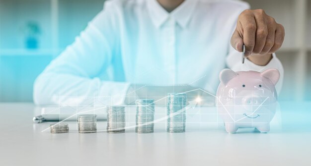 A person puts a coin in a pig piggy bank, a large number of coins are placed on the table from low to high, chart graphics showing the financial situation. concept of personal finance management