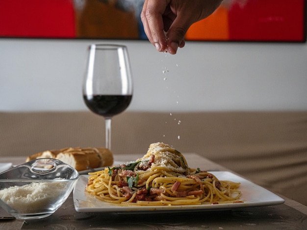 Person putting cheese on the pasta with bread cheese and glass of wine