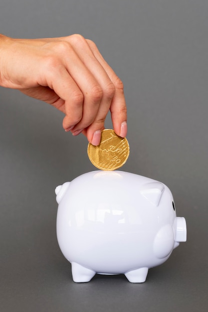 Person putting in white piggy bank coins