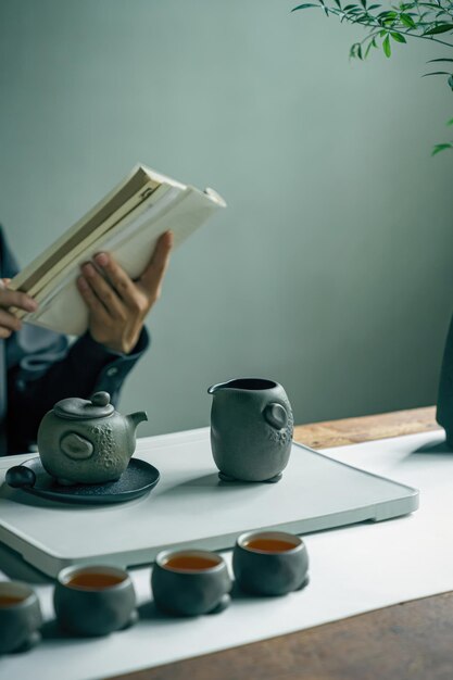 A person reading a book in front of a pot of tea.