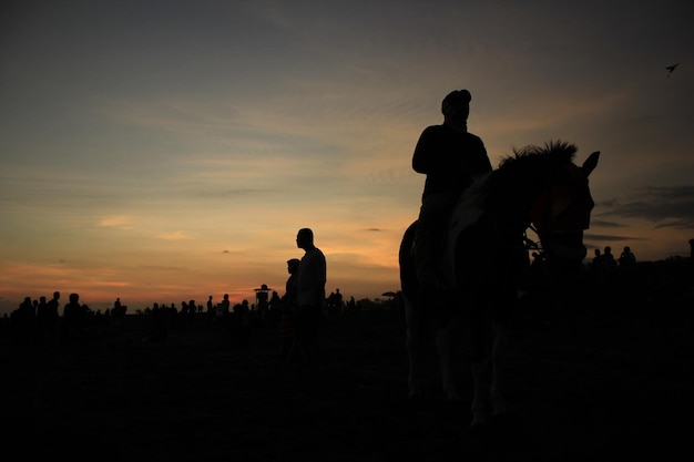 A person riding a horse in front of a sunset with a person on the horse.