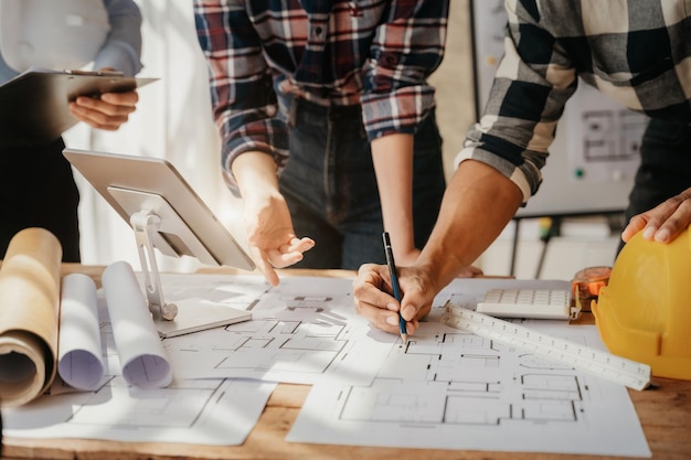 Person\'s engineer hand drawing plan on blue print with\
architect equipment architects discussing at the table team work\
and work flow construction concept