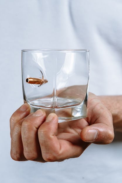 A person's hand holding a clear glass with a bullet stuck in it