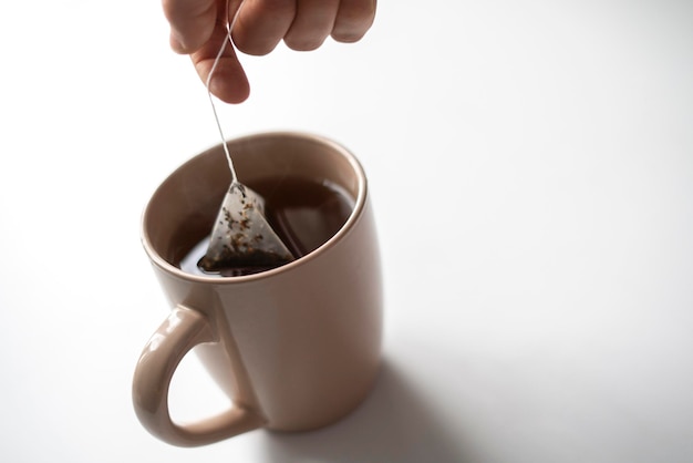 A person's hand holding a tea bag and making hot cup of tea