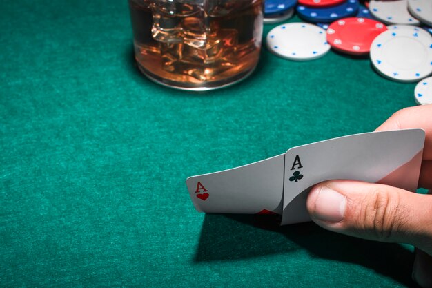 Photo a person's hand holding two aces heart shape and club card on poker table