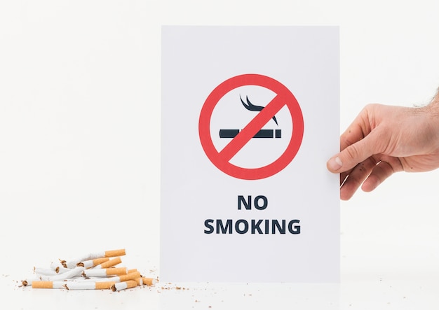 Photo a person's hand showing no smoking sign near the broken cigarettes on white background