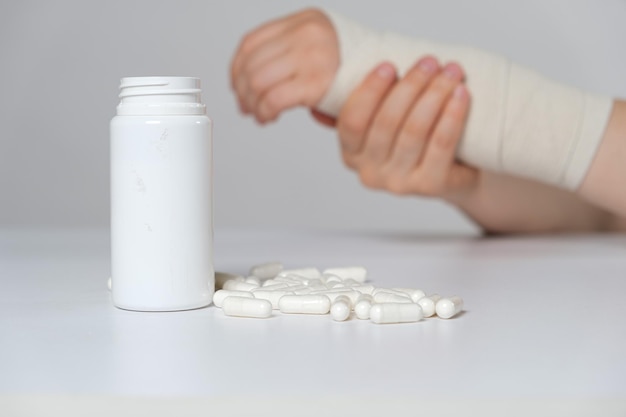 A person's hand with an elastic bandage and a jar of calcium or chondroitin tablets