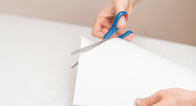 A person's hands holding piece of paper sheet and cut it with scissors