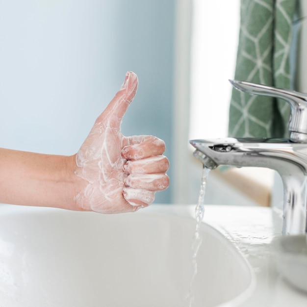 Photo person showing thumbs up while washing their hands in the bathroom