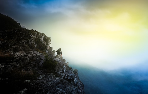 person sitting on cliff against sky during sunset