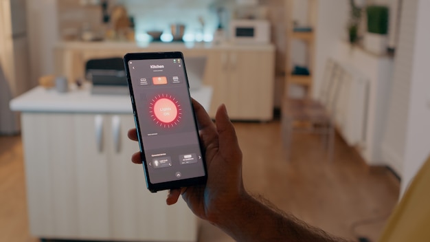 Person sitting in house with automation light system holding smartphone turning on bulbs, controlling wireless room ambiance with smart home application. Mobile with modern software app