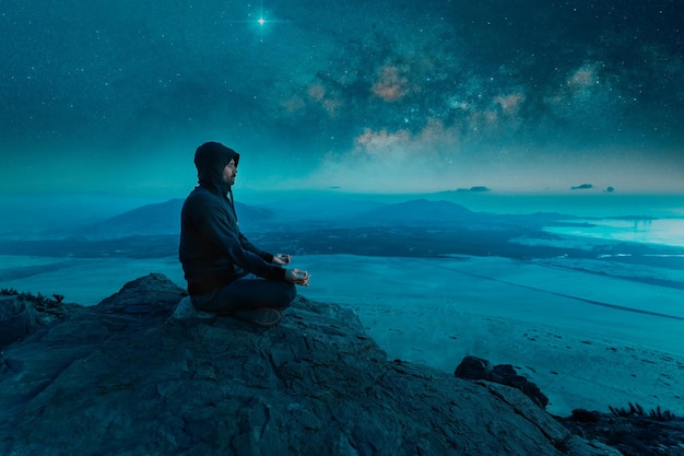 Фото Человек, сидящий на вершине горы и медитирующий ночью со звездами и фоном млечного пути