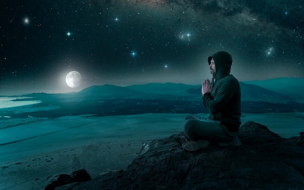 person sitting on the top of the mountain meditating or contemplating the starry night