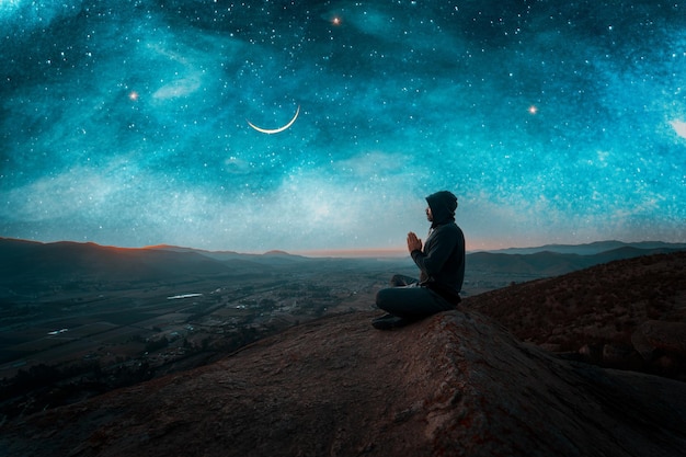 Person sitting on the top of the mountain meditating or contemplating the starry night