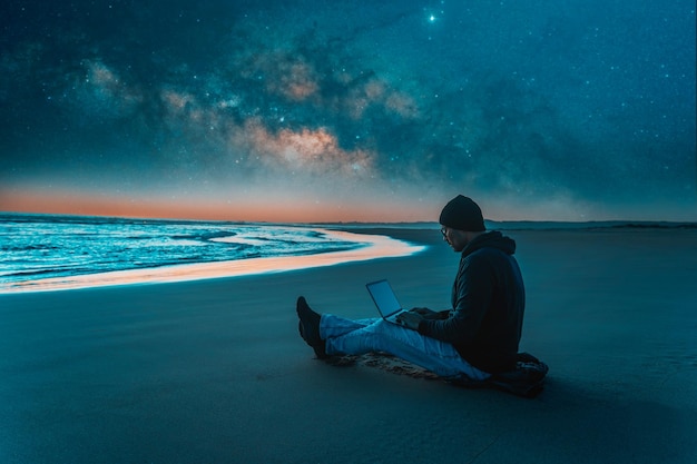 Person sitting with laptop on the beach outdoors working under the starry night and milky wayx9