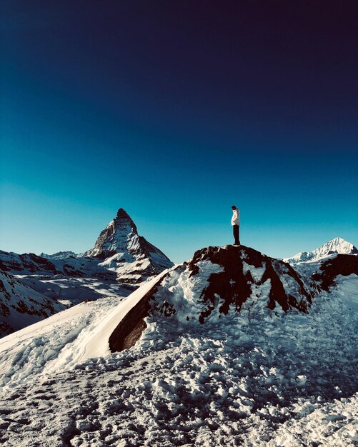 Person on snowcapped mountain against clear blue sky