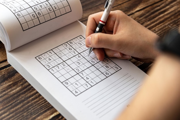 Person solving a sudoku puzzle on a wooden table