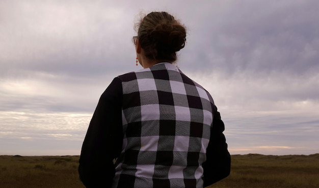 Person standing on grassy field against cloudy sky