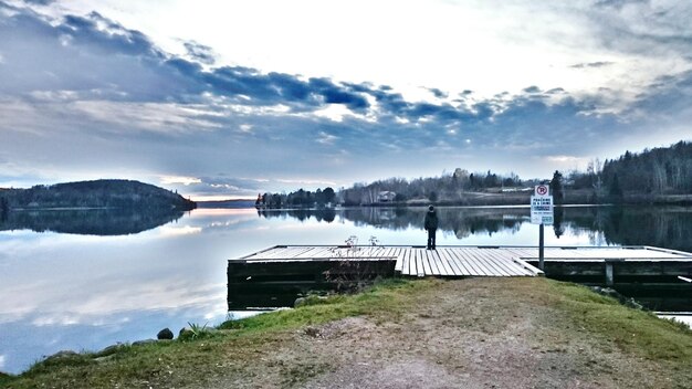 Foto persona in piedi sul molo vicino al lago contro il cielo