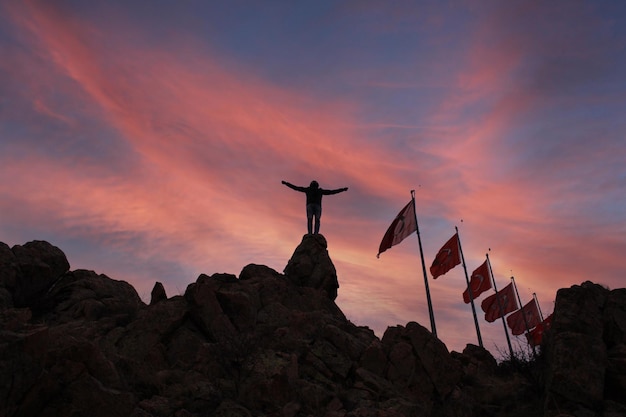 A person stands on a mountain with flags on the top.