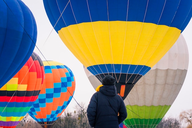 Человек стоит спиной и смотрит на разноцветные воздушные шары, летящие в небе.