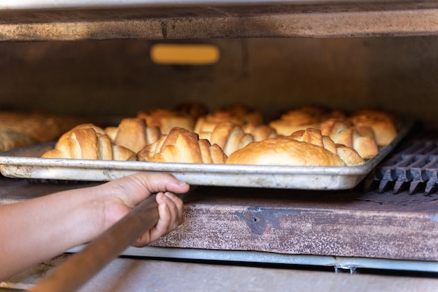 Photo person taking pastries out of an industrial oven
