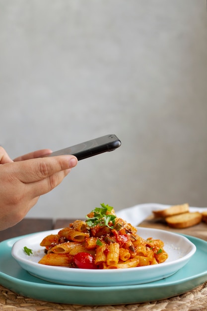 Foto persona che scatta foto del piatto di pasta con lo smartphone