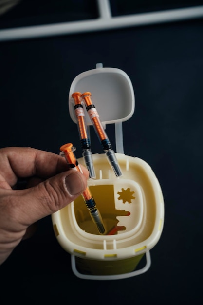 A person throwing a syringe into a medical waste container