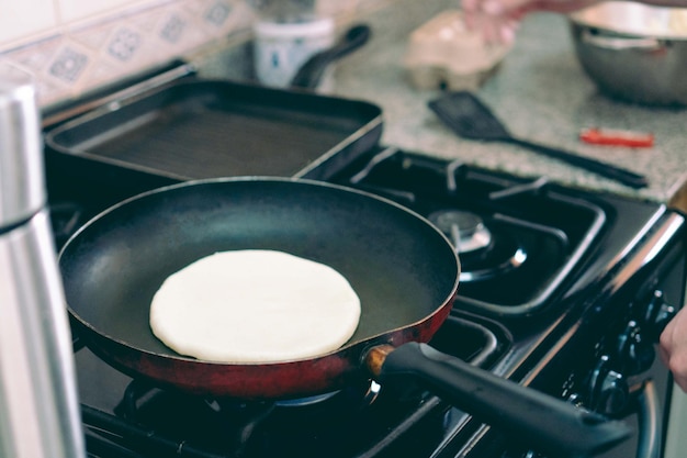 Person turning on the stove to heat an arepa in a frying pan