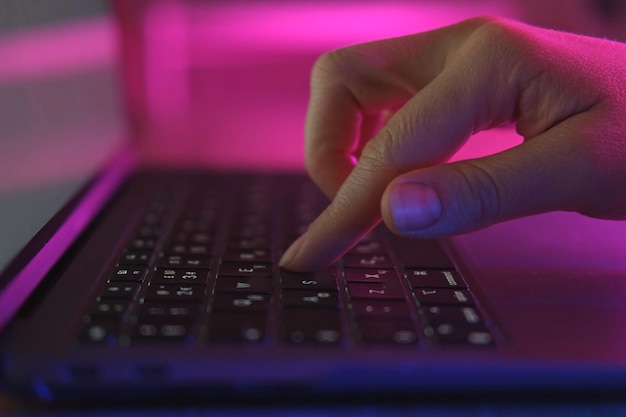 person typing at laptop computer at night female uses keyboard shakes buttons with fingers internet security cyber attack trendy neon light creative vivid color of ultraviolet red and blue