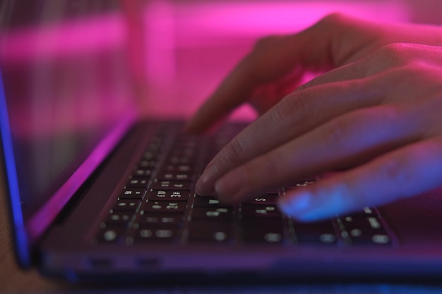 Person typing at laptop computer at night Female uses keyboard shakes buttons with fingers Internet security cyber attack Trendy neon light Creative vivid color of ultraviolet red and blue