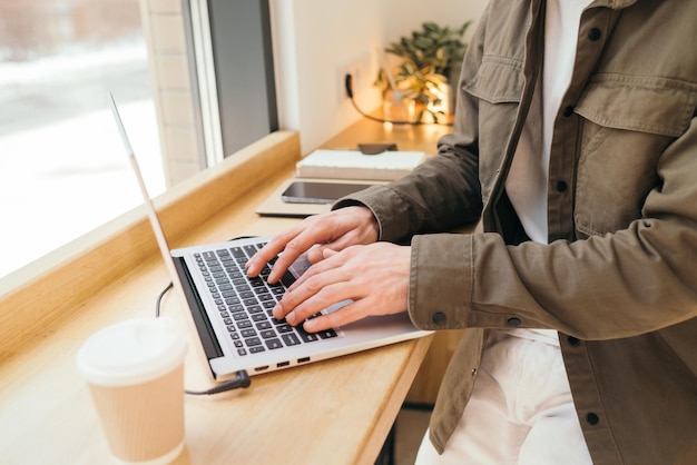 A person typing on a laptop with a coffee cup in the background.