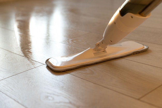 Person using spray mop pad and refillable bottle with cleaning solution, mopping the floor in apartment