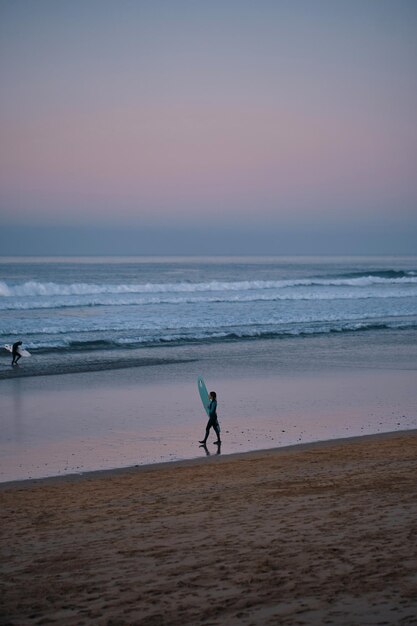 A person walking on a beach with a surfboard in hand.