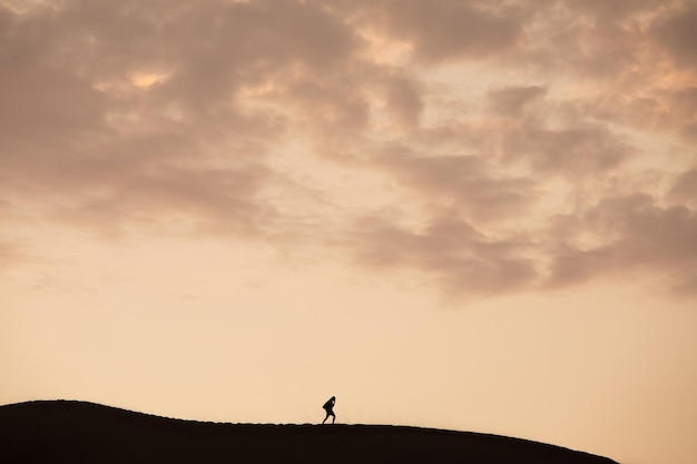 Person walking on the top of a dune in Ica Peru during sunset