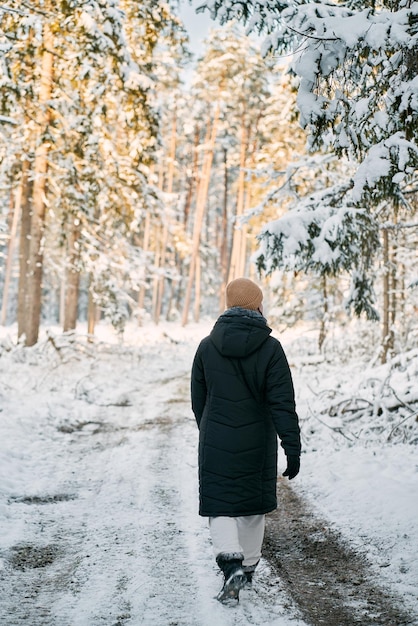 A person walks on the winter road no face woman hiking in a\
snowcovered forest