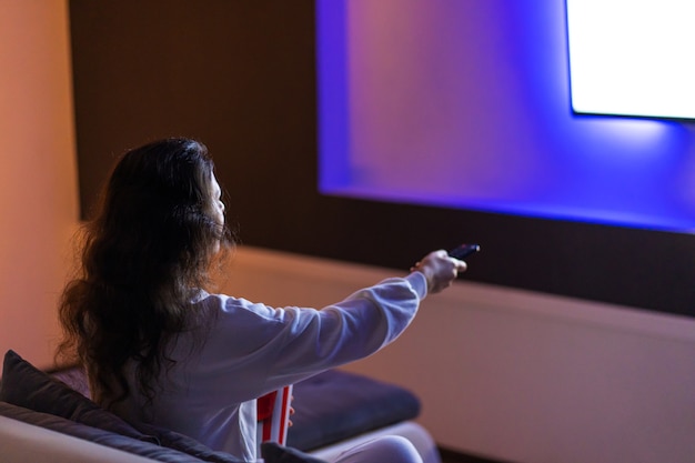 La persona guarda un film seduta sul divano con un secchio di popcorn.