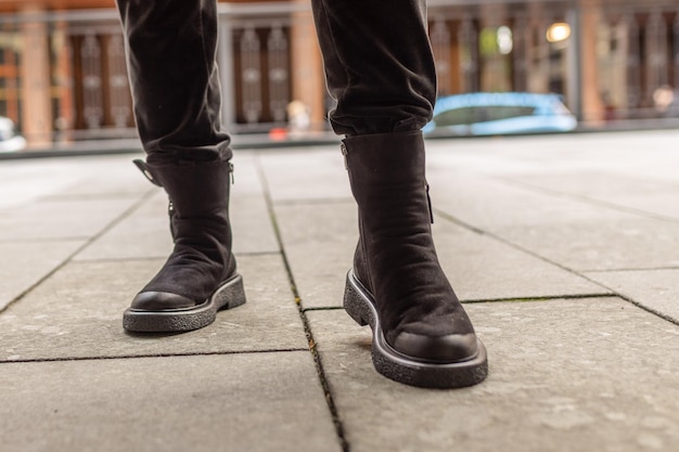 A person wearing black boots stands on a sidewalk.