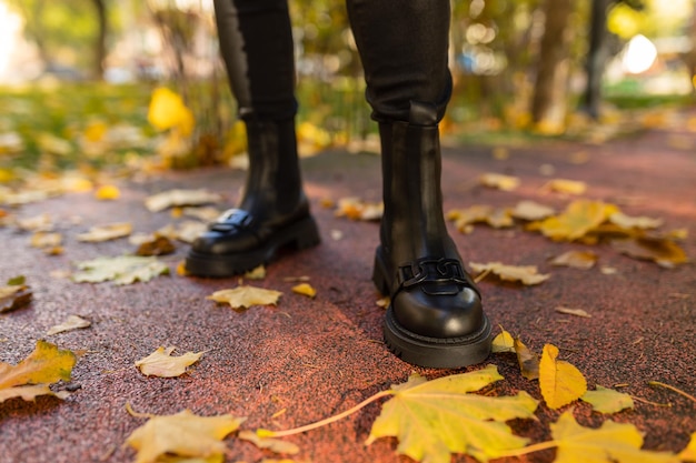 A person wearing black boots stands on a wet ground with autumn leaves on the ground.