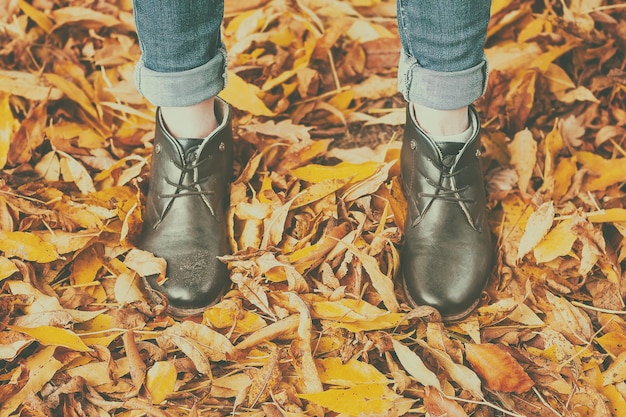 A person wearing black shoes and jeans stands in a pile of leaves