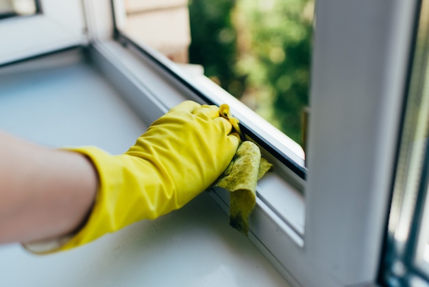 A person wearing gloves washes the window frame with a cleaning cloth.