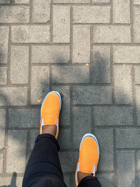 A person wearing orange shoes stands on a sidewalk.