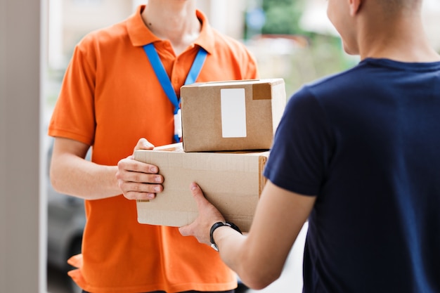 オレンジ色のTシャツと名札を着た人が荷物をクライアントに配達しています。フレンドリーな労働者、高品質の配達サービス。