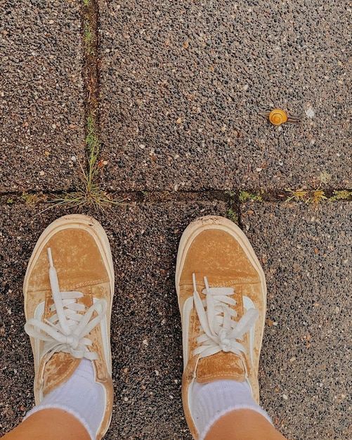 A person wearing a pair of dirty shoes stands on a sidewalk.