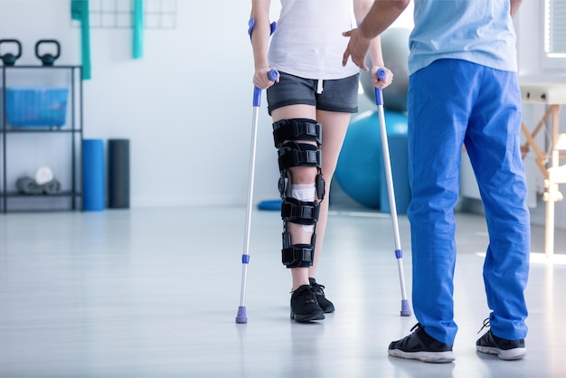 Photo a person with a leg brace is walking with a patient in a hospital.