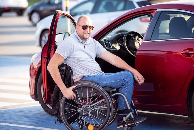 Persona con disabilità fisica che sale su un'auto rossa dalla sedia a rotelle