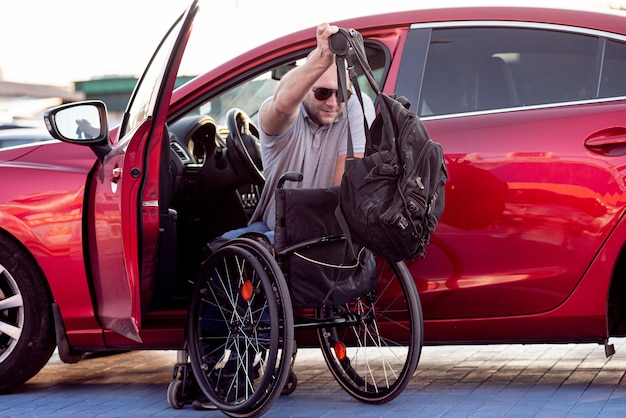 Человек с ограниченными физическими возможностями, садясь в красный автомобиль с инвалидной коляски