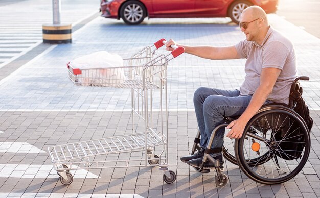 Человек с ограниченными физическими возможностями толкает тележку перед собой на парковке супермаркета